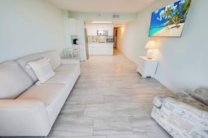 A modern living room with a sofa, a small table, and a kitchen in the background.