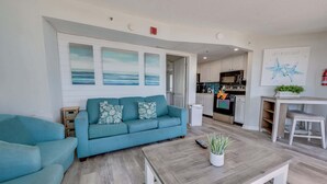 A living room with a sofa, a coffee table, and a kitchen in the background.