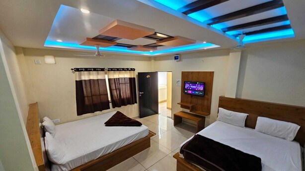 Una moderna camera d'hotel con due letti, una TV a schermo piatto fissata al muro e un soffitto illuminato con luci LED blu.