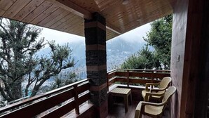 A wooden deck with a stone pillar, wooden benches, and wicker chairs. - Godfather By GRB (Manali)
