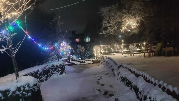 A snow-covered pathway leading to a seating area with string lights. - Godfather By GRB (Manali)