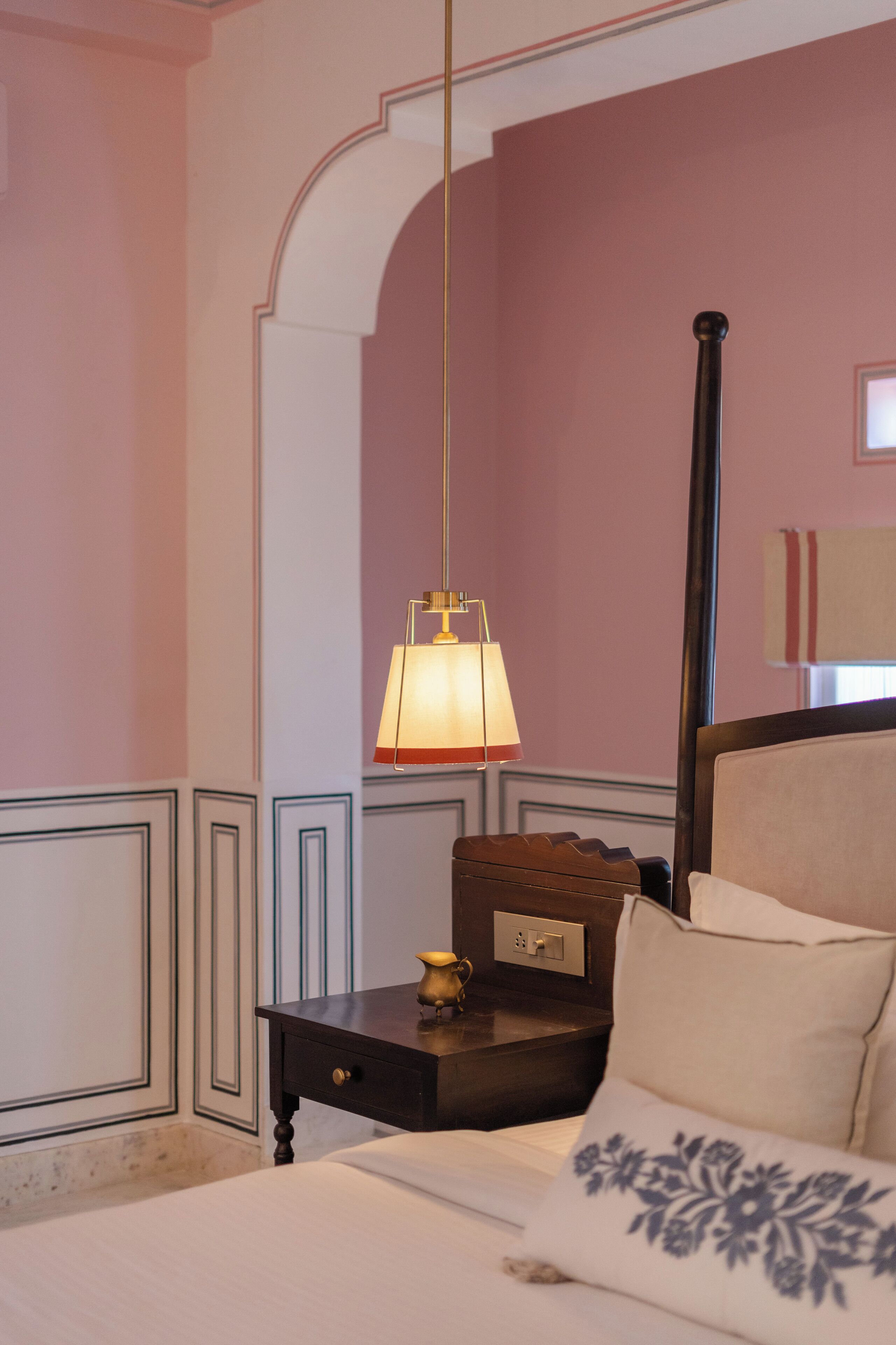 A hotel room with a bed, a nightstand, a lamp, and a mirror.