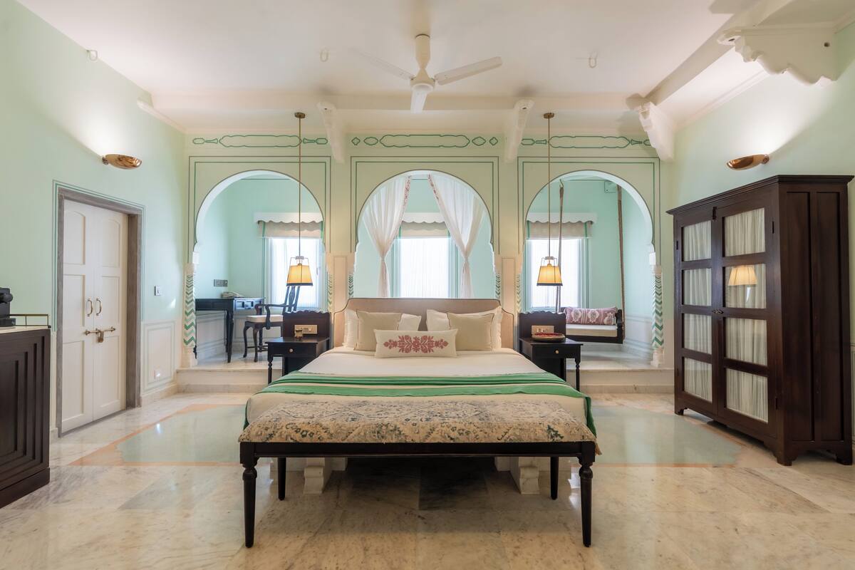 A spacious bedroom with a large bed, a ceiling fan, and a view of the adjacent room through an arched doorway.