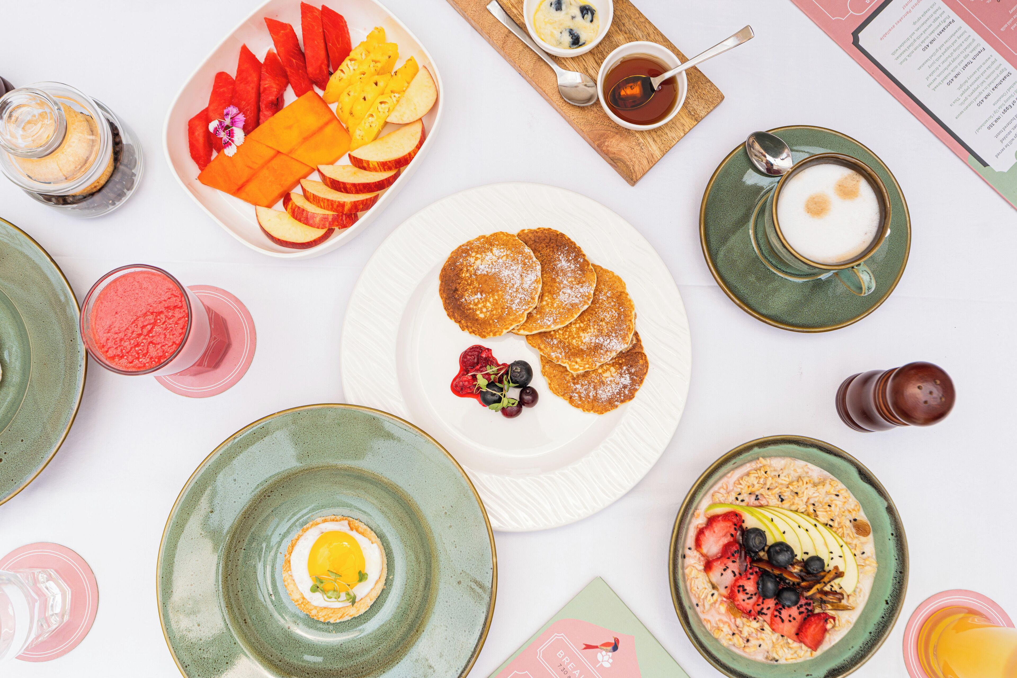 A breakfast setting with various dishes, including pancakes, fruit, and beverages.