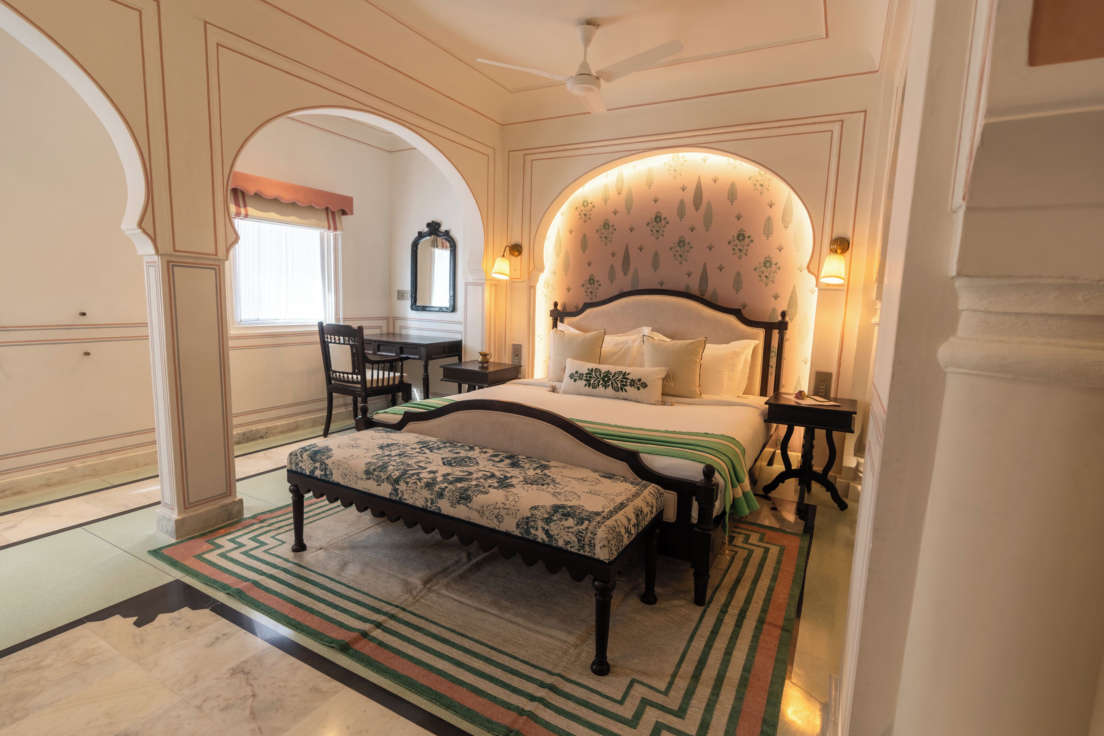 A bedroom with a large bed, a bench, a desk, and a chair.