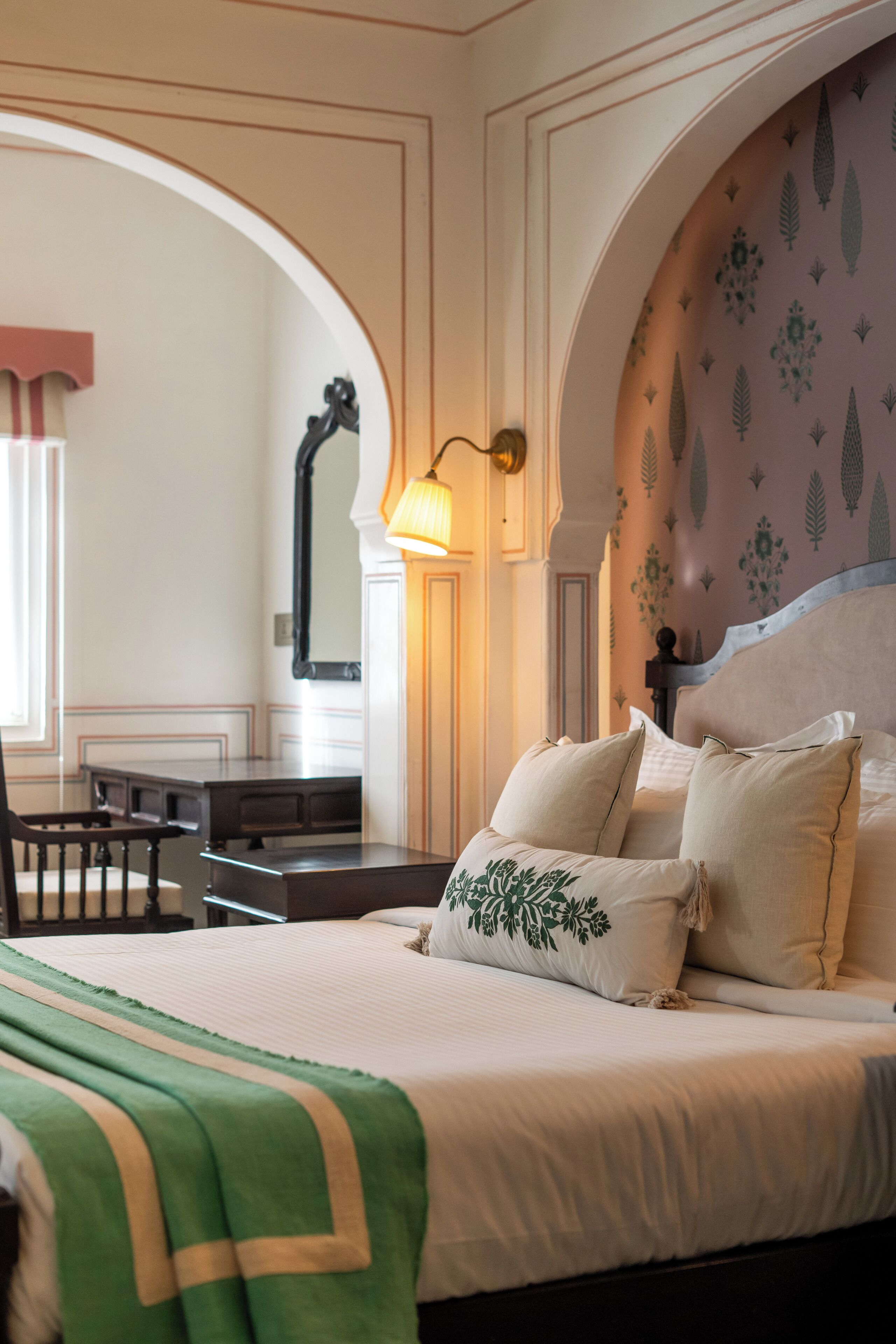 A hotel room with a large bed, a desk, and an arched doorway.
