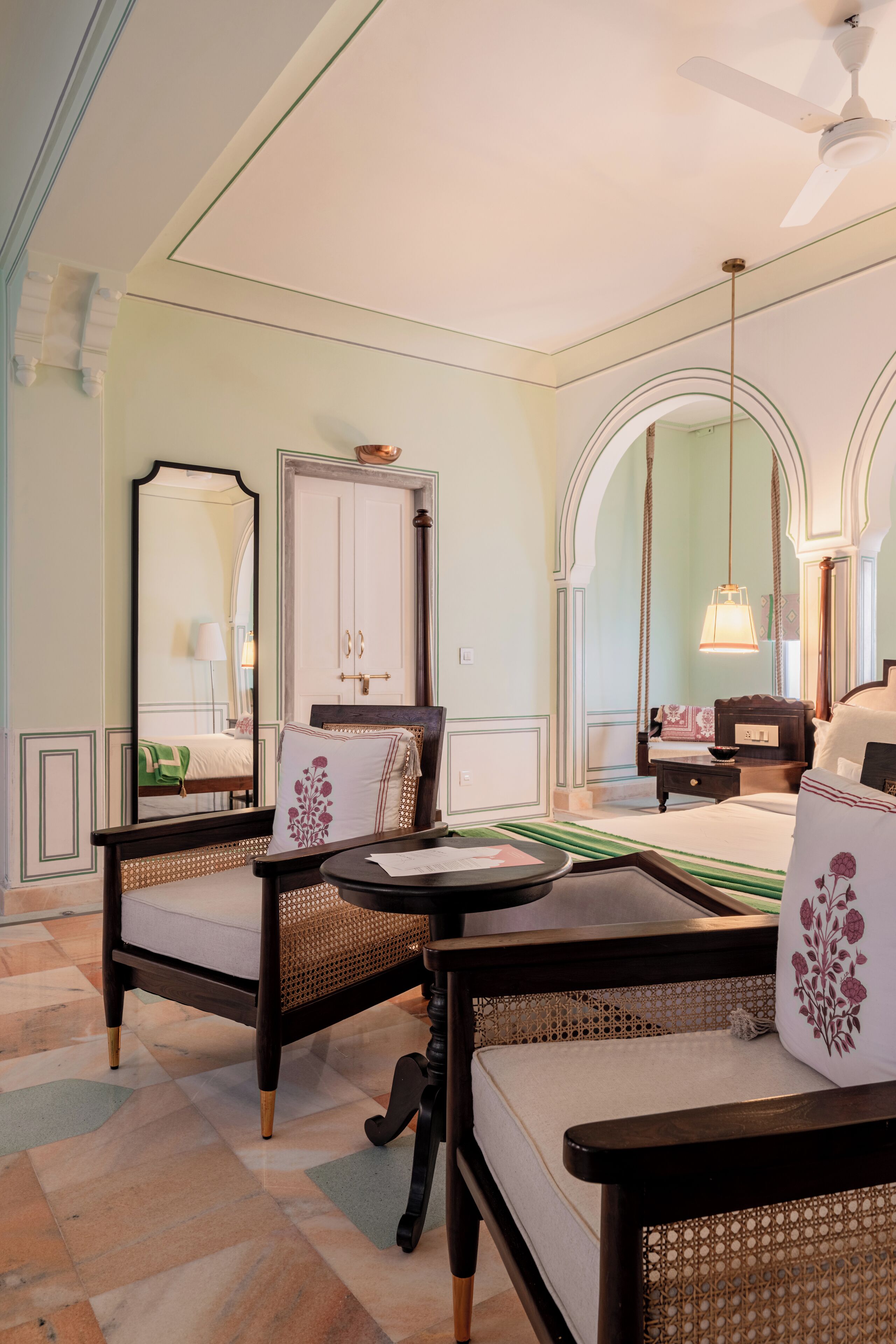 Habitación de hotel con cama, dos sillones, una mesita, un espejo y un ventilador de techo.