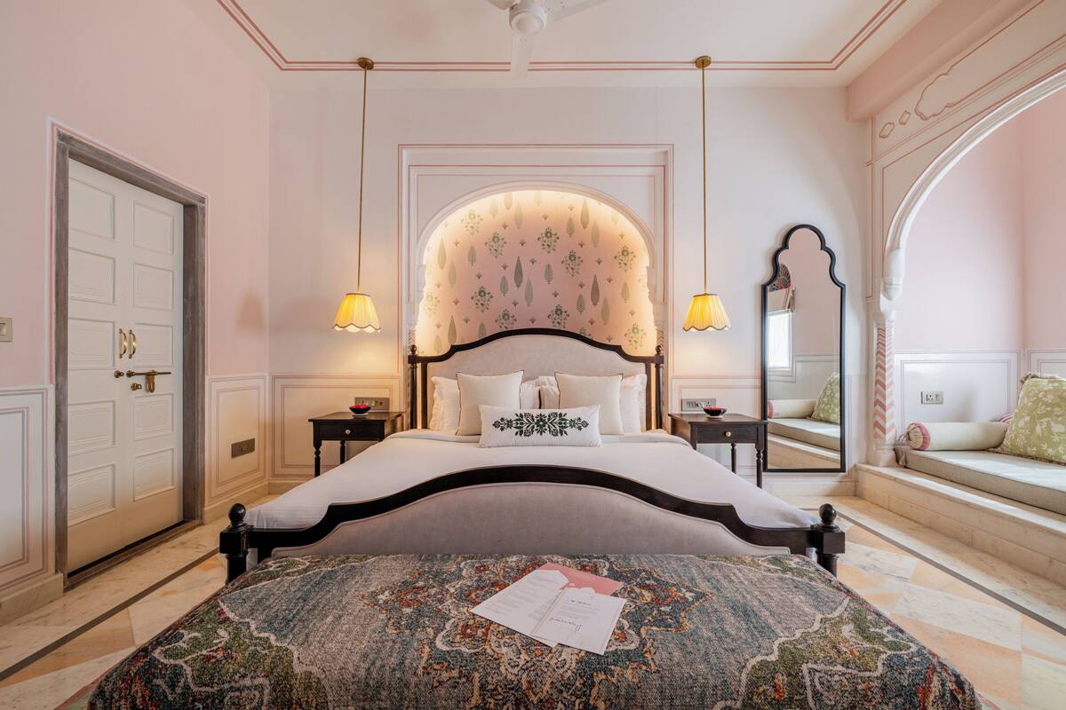 A bedroom with a large bed, two bedside tables, a mirror, and a bench by the window.