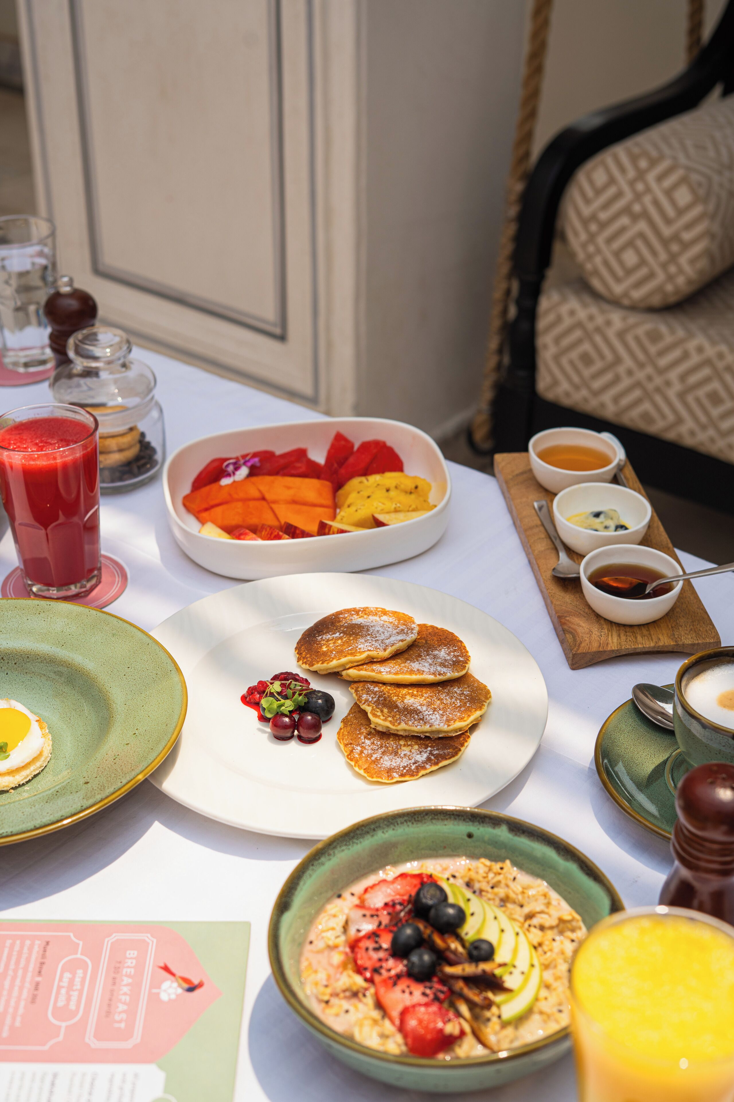 Una mesa de desayuno con diferentes platos, como tortitas, fruta y un tazón de avena.