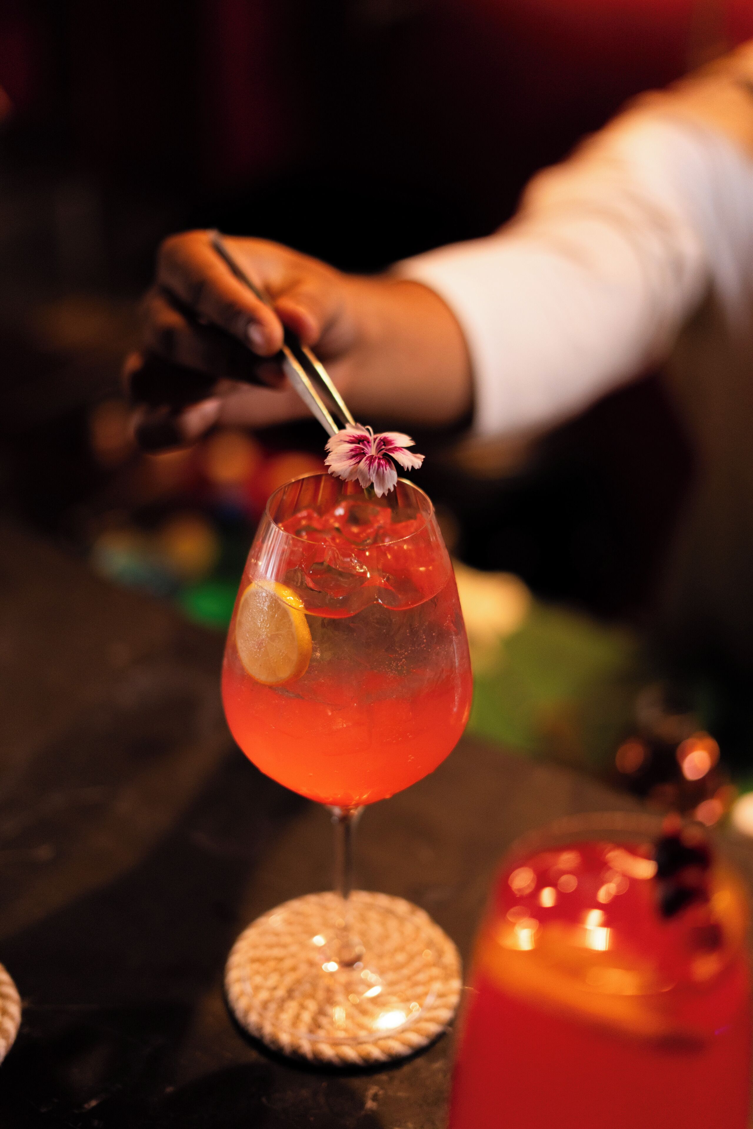 A cocktail with a lemon slice and a flower garnish on a glass with a stem.
