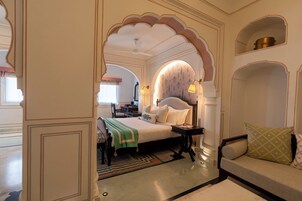 A traditional room with a bed, a sofa, and a small table. There are decorative arches and a ceiling fan.