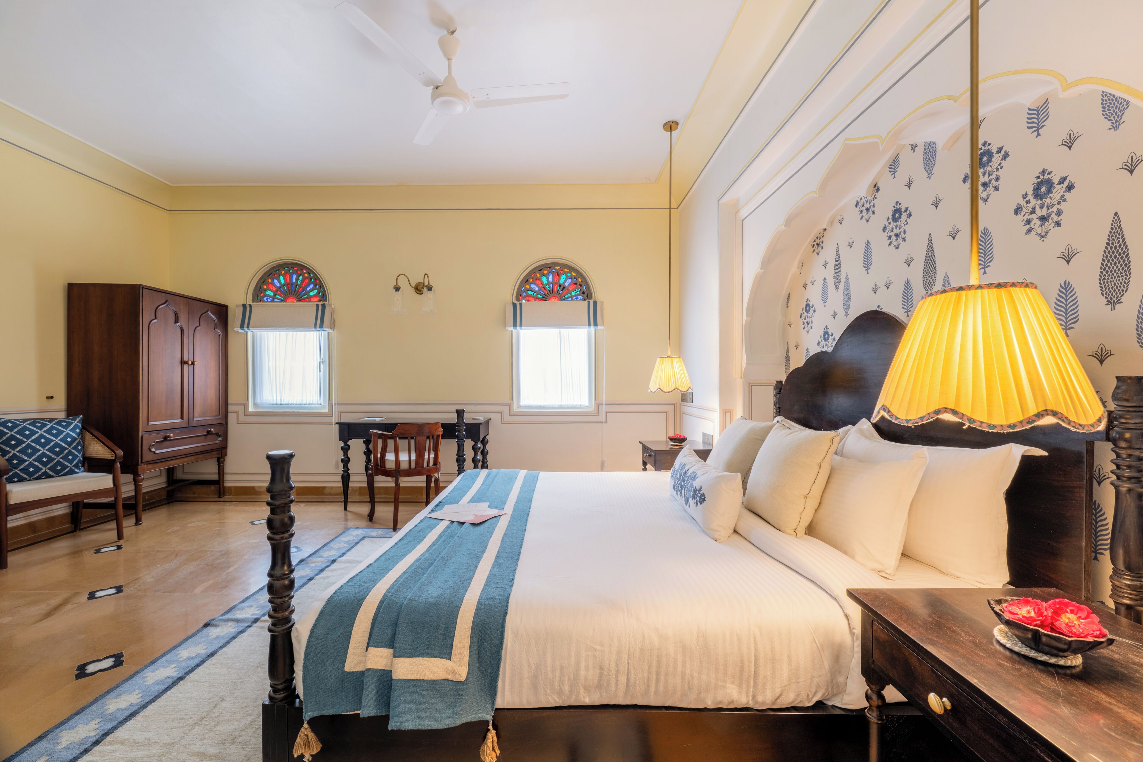 Un dormitorio con una cama grande, un armario de madera, dos ventanas con vidrieras, un escritorio y una silla.