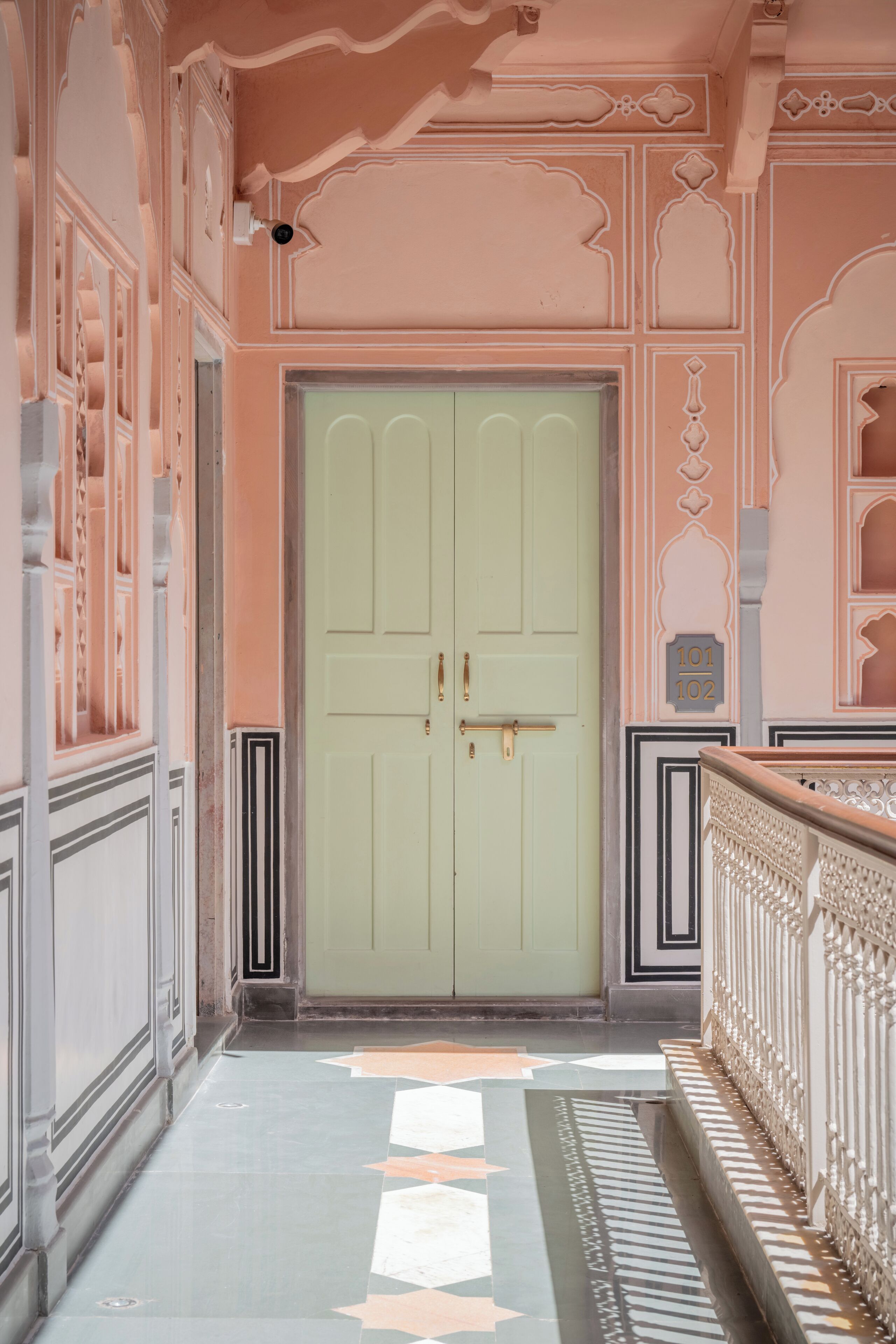 A hallway with a light green door, ornate wall decorations, and a patterned floor.