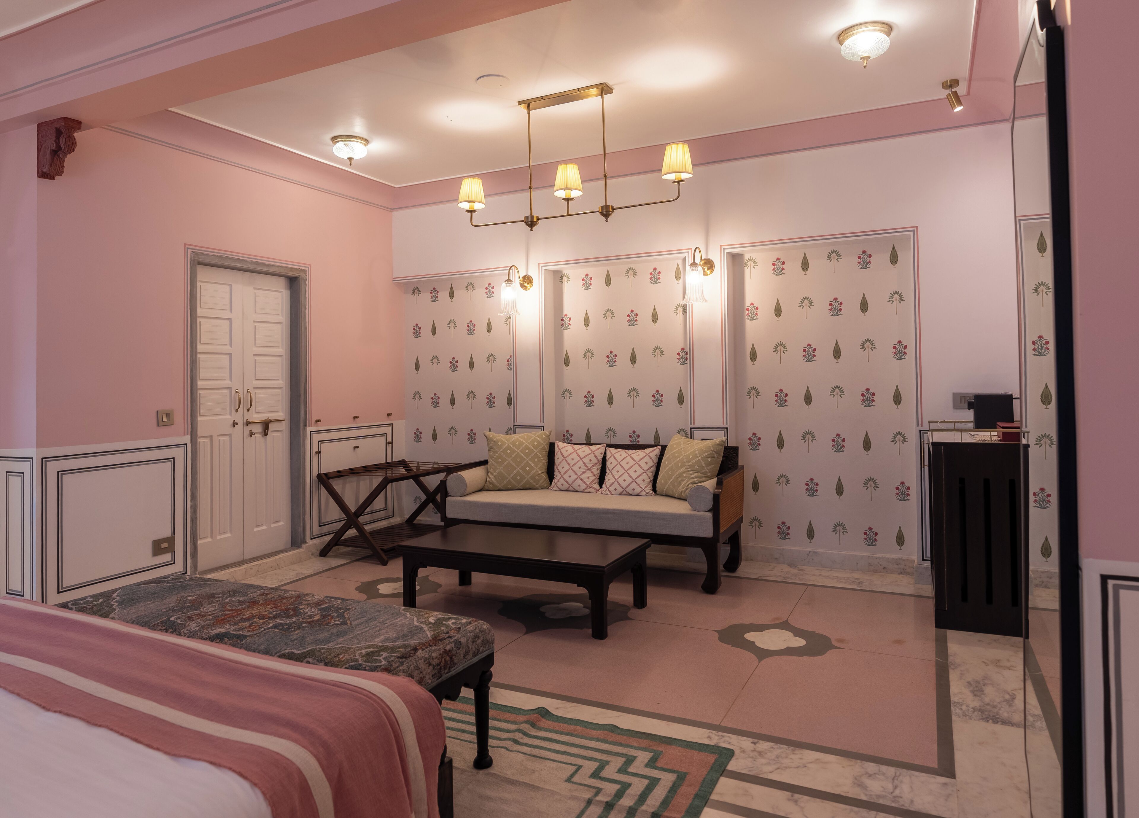 Una habitación con cama, sofá, mesa de centro, escritorio y papel tapiz estampado.