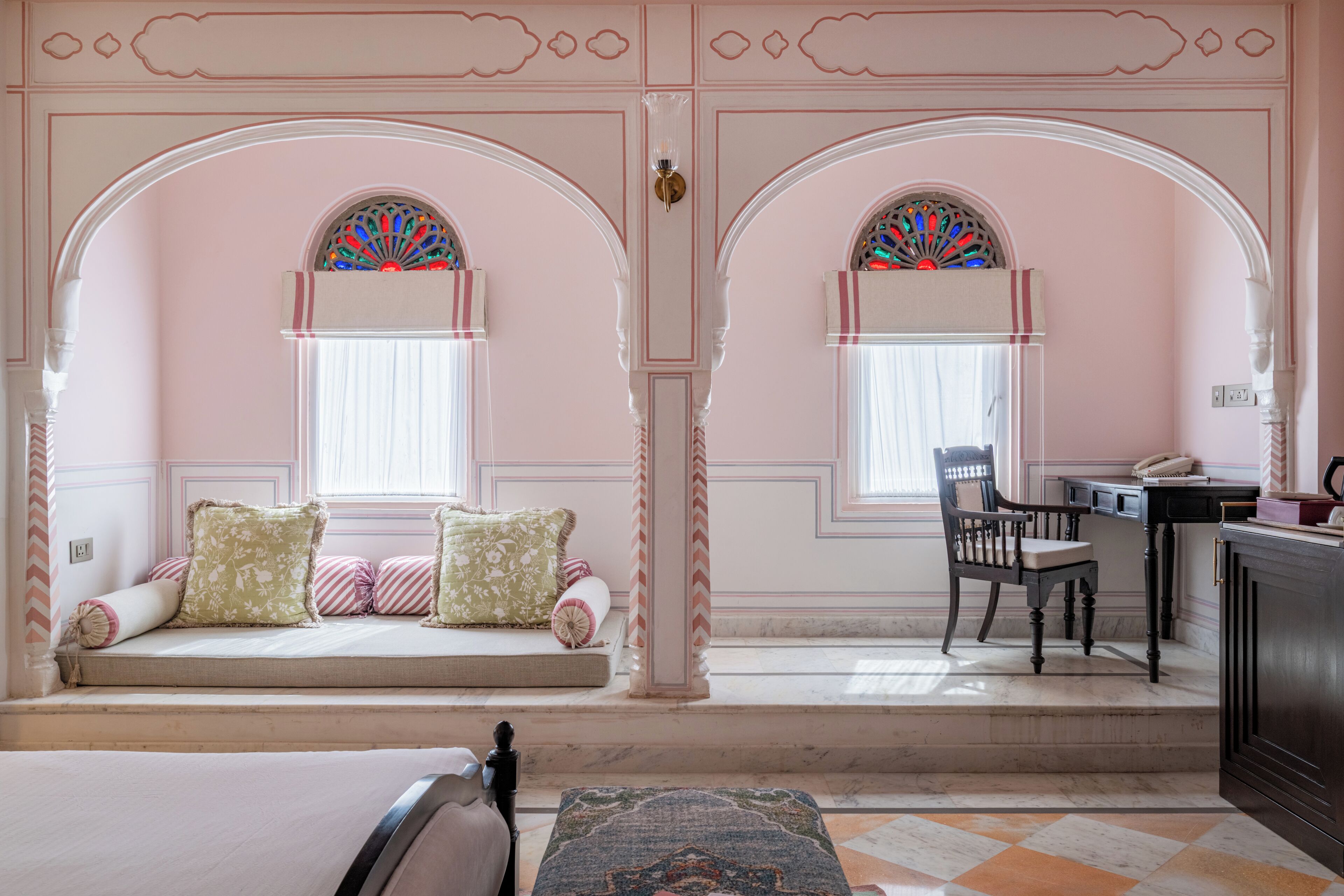 A room with a bed, a desk, and a chair. There are two windows with decorative glass.