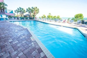 Une piscine dont la profondeur maximale est de 3 pieds, entourée de chaises longues et de palmiers.