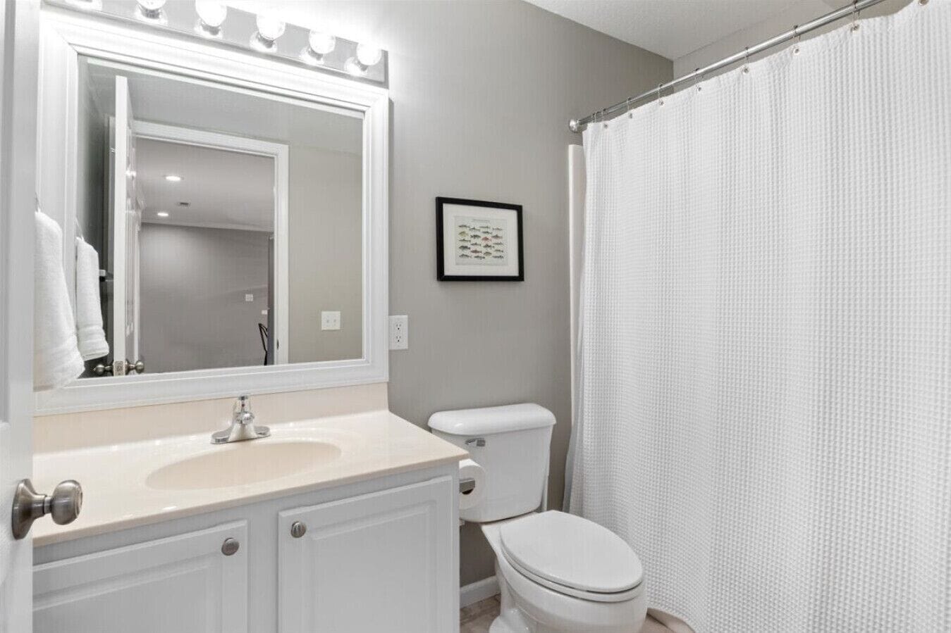Une salle de bain avec un meuble-lavabo, des toilettes, un rideau de douche et un tableau encadré au mur.