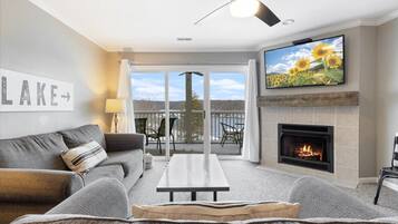 A living room with a sofa, a coffee table, a fireplace, a television, and a view of a lake.