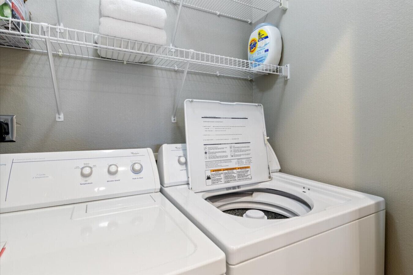 A laundry area with a front-loading washer and dryer, a shelf with laundry detergent, and a white wall.