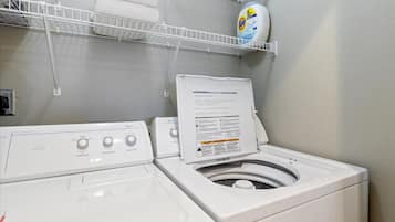 A laundry area with a front-loading washer and dryer, a shelf with laundry detergent, and a white wall.