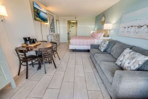 Ein Hotelzimmer mit einem Bett, einem grauen Sofa, einem Esstisch mit Stühlen und Kunstwerken an den Wänden.