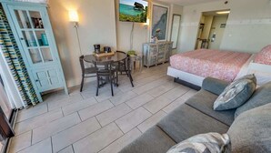A hotel room with a bed, a sofa, a dining table with chairs, a TV mounted on the wall, and a cabinet.
