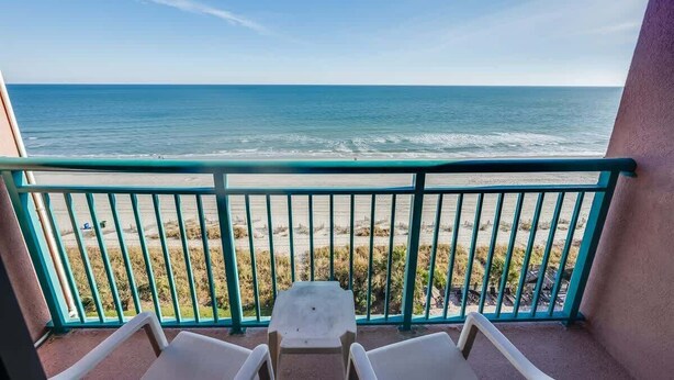 A balcony with a view of the ocean, a small table, and two chairs.