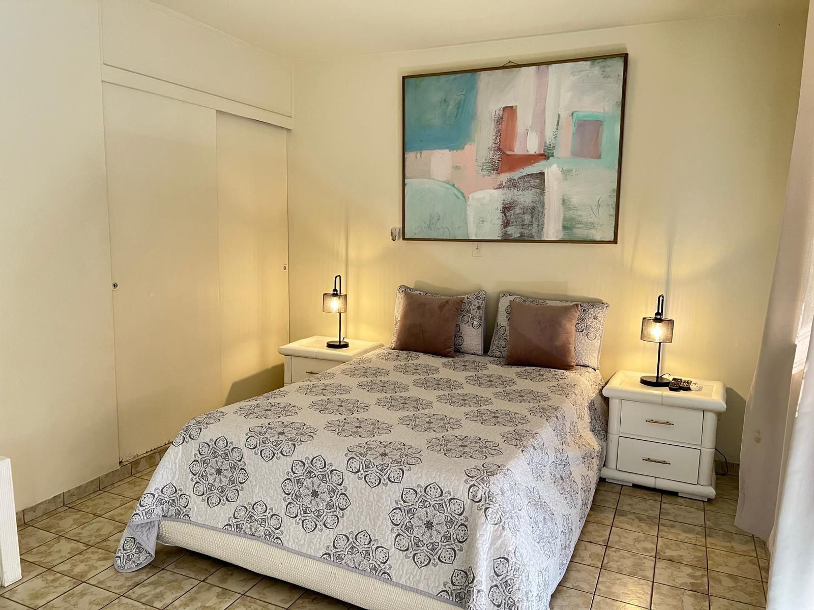 Un dormitorio con cama, dos mesitas de noche, una mesilla auxiliar, un cuadro y una puerta.