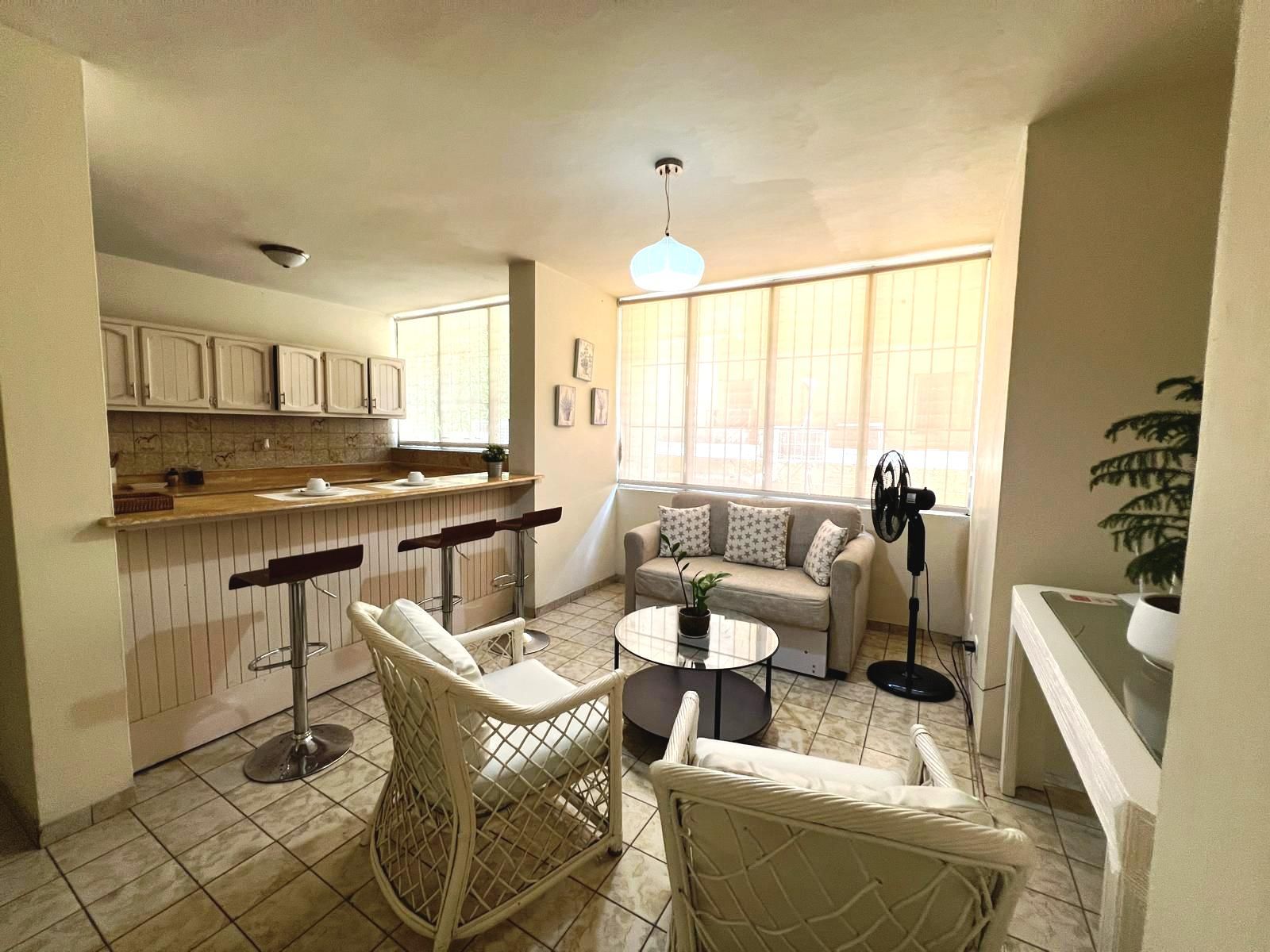 A compact living space with a kitchenette, a dining area with chairs, a sofa, and a fan.