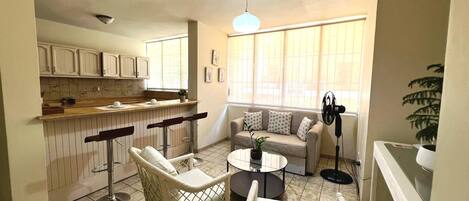 A compact living space with a kitchenette, a dining area with chairs, a sofa, and a fan.