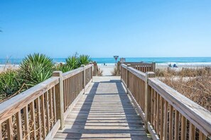 A wooden boardwalk leading to a beach with clear skies.