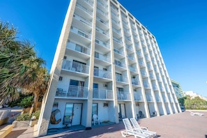 A multi-story hotel with balconies, a pool area, and a clear blue sky.