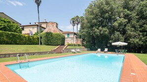 A rectangular swimming pool with a tiled edge, surrounded by a brick patio. There are lounge chairs and a small umbrella on the patio. - Villa Ott in Crespina (Lorenzana)