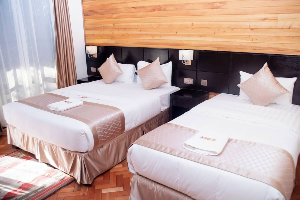 Habitación de hotel con dos camas, cada una con cabecero, mesitas de noche y una ventana con cortinas.
