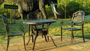 A table and two chairs in an outdoor setting with a sign reading "Kambi Mstuni Resort" and an elephant in the background. - Kambi Mstuni Resort (Ndaragwa)