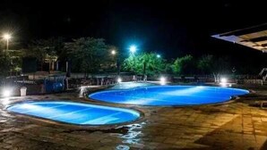 A nighttime view of a swimming pool area with multiple pools, surrounded by a stone patio and illuminated by street lamps. - Kambi Mstuni Resort (Ndaragwa)