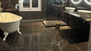 Un baño moderno con bañera, dos lavamanos, una ventana y un espejo con luces circulares, fijado a la pared.