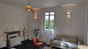 Una habitación con chimenea, un sofá, una silla, una lámpara y una ventana con vistas a la vegetación.
