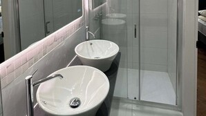 Een moderne badkamer met twee wasbakken, een douchecabine van glas en een grote spiegel.