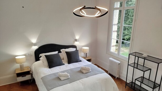 Een keurig opgemaakt slaapkamer met een bed, nachtlampjes, een radiator en een raam met uitzicht.