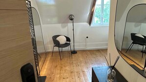 Een kamer met een schuine plafond, houten vloer, een stoel, een vloerlamp, een spiegel en een tafeltje met een kaars.