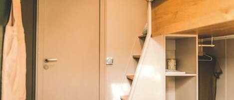Una habitación con una escalera de madera que conduce a un armario con estantes y espacio para colgar.