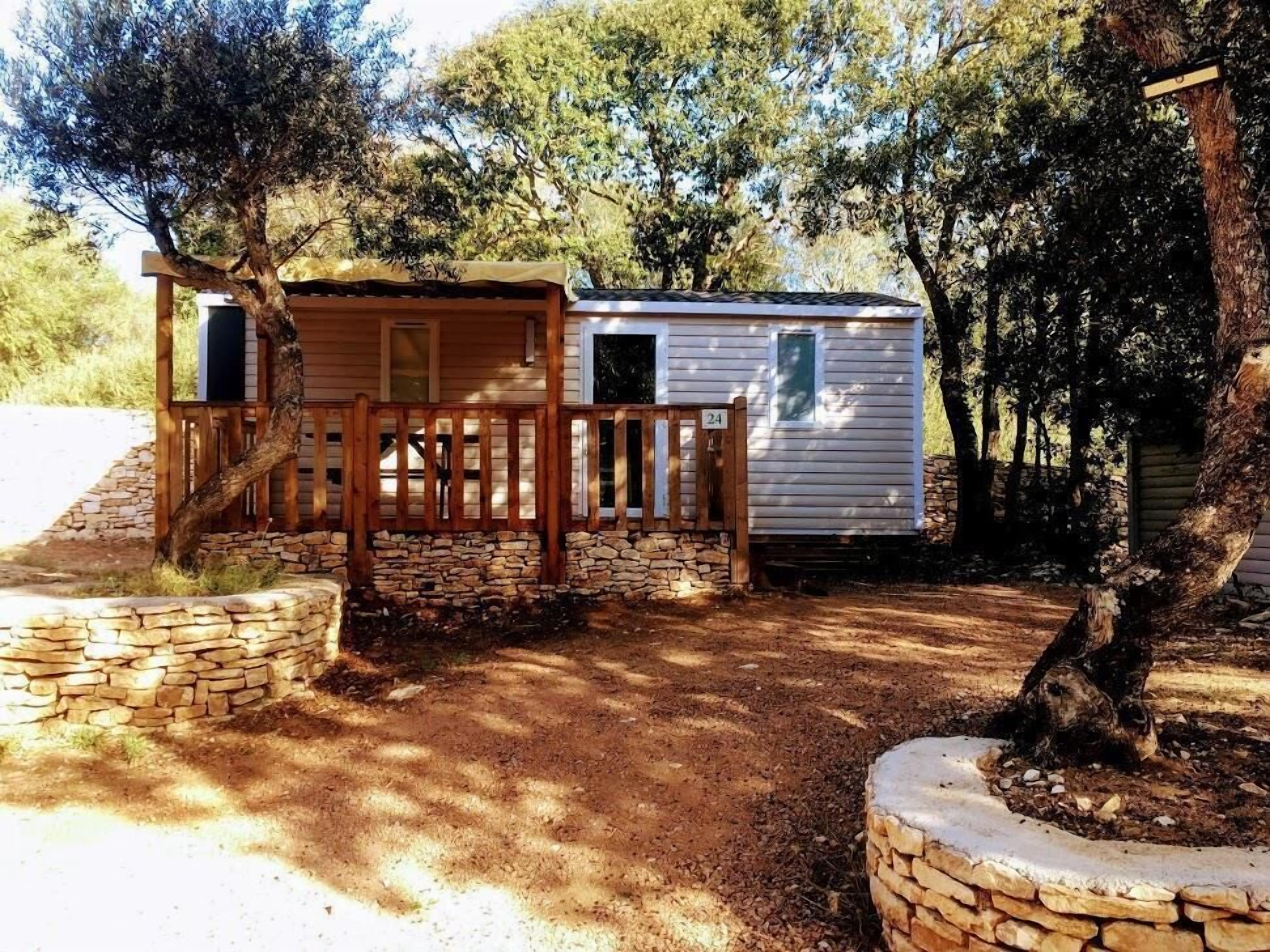 Une petite cabane dotée d’une terrasse en bois et de murs en pierre, entourée d’arbres.