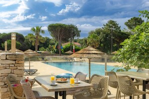 Zona de comedor junto a la piscina con una mesa para dos, un pilar de piedra y vistas a la piscina y la vegetación circundante.