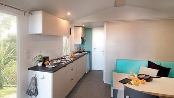A compact kitchen with a central island, a dining area with a teal sofa, and a view of greenery outside.