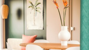 Een eetgedeelte met een ronde houten tafel, witte stoelen en een witte vaas met oranje bloemen.