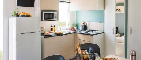 A compact kitchen with a refrigerator, microwave, and stove. There is a dining table with chairs and a basket of bread.