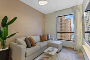 A modern living room with a beige sofa, a coffee table, and a large window with curtains.