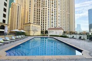 A swimming pool with lounge chairs and umbrellas, surrounded by high-rise buildings.