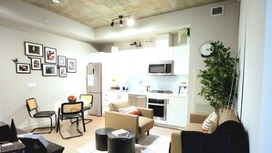 Un salon moderne avec un canapé, une table basse et des fauteuils. Il y a également un coin cuisine équipé d’un four à micro-ondes et d’une cuisinière.